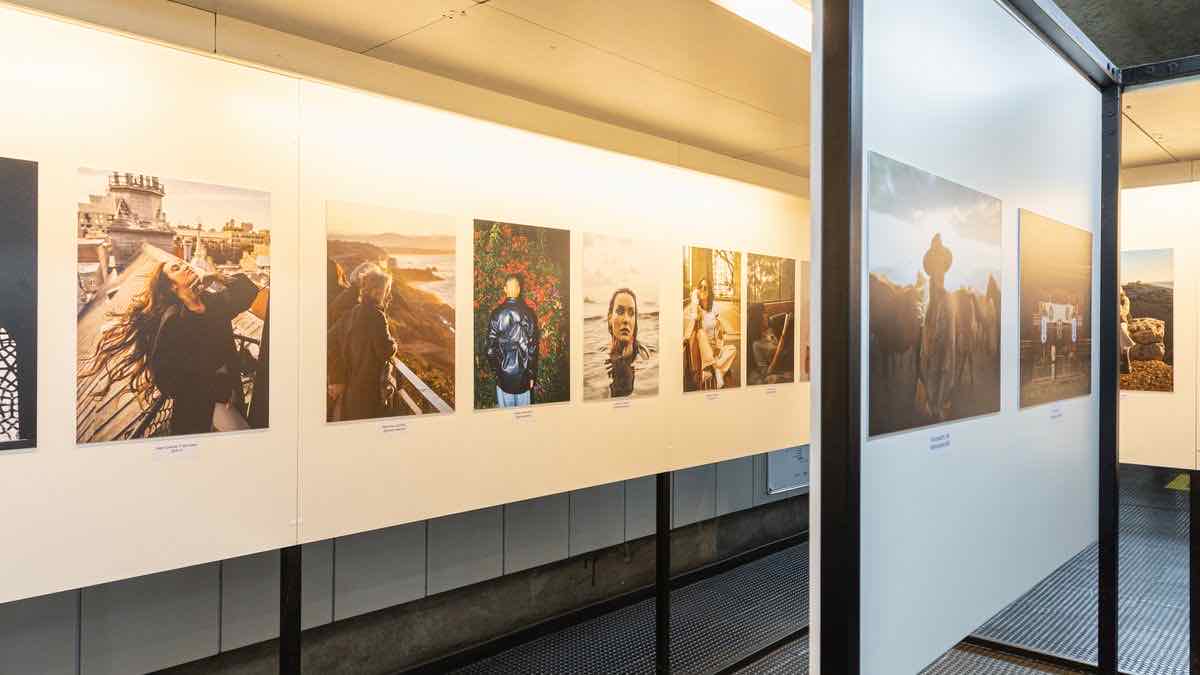 A lit exhibition corridor with large photographic prints hung in a row and a caption beneath each one
