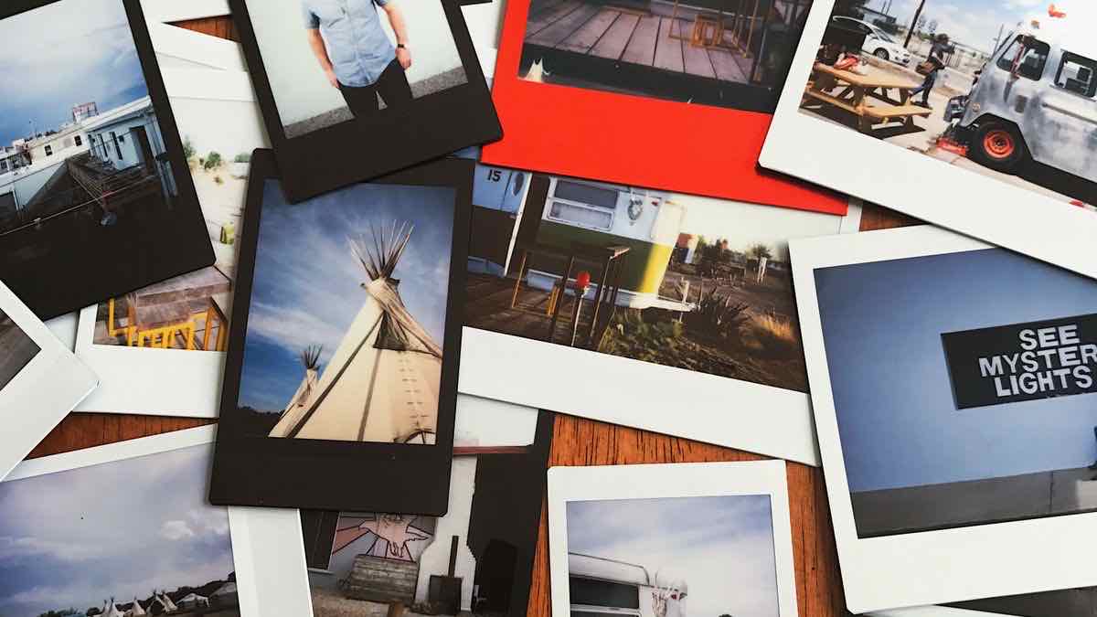 A scattered pile of instant prints showing road-trip scenes, with a photograph of a tipi lying on top of the pile