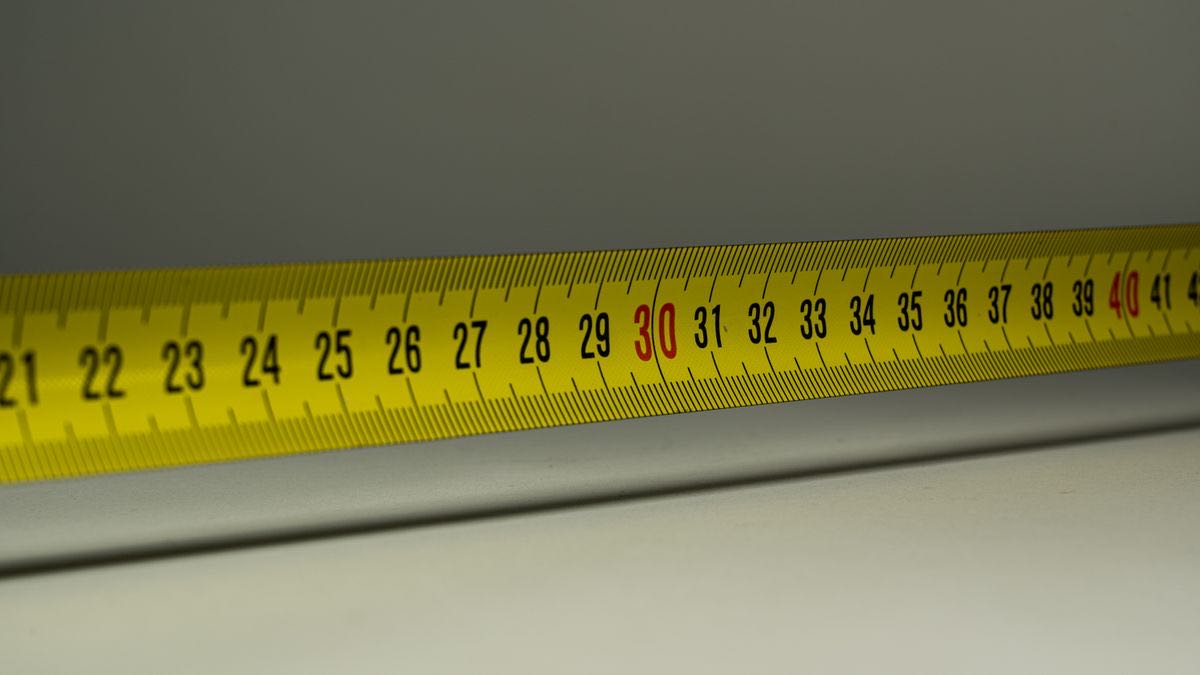 A yellow steel tape measure extended across a grey surface with the numbers 21 to 42 legible and 30 and 40 printed in red