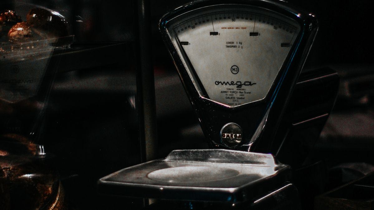 An old brass shop scale lit in a dark storefront, the merchant's own instrument for weighing what they sell