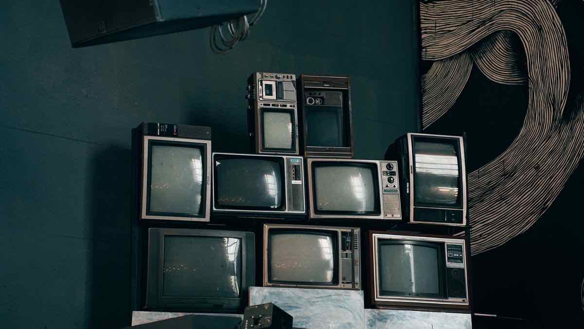A pyramid of a dozen switched-off CRT televisions stacked against a dark teal wall, standing in for a stack of video search products that all look the same until you switch one on