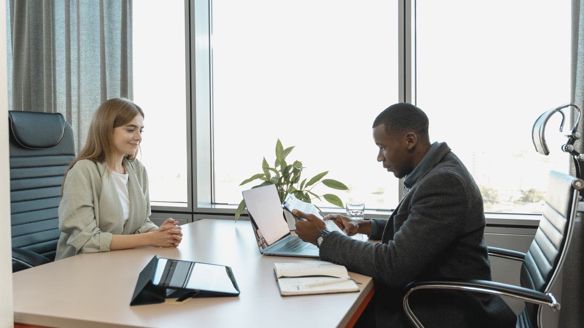 A recruiter reviewing a document across the desk from a candidate in a bright office, the human review step that follows automated sourcing