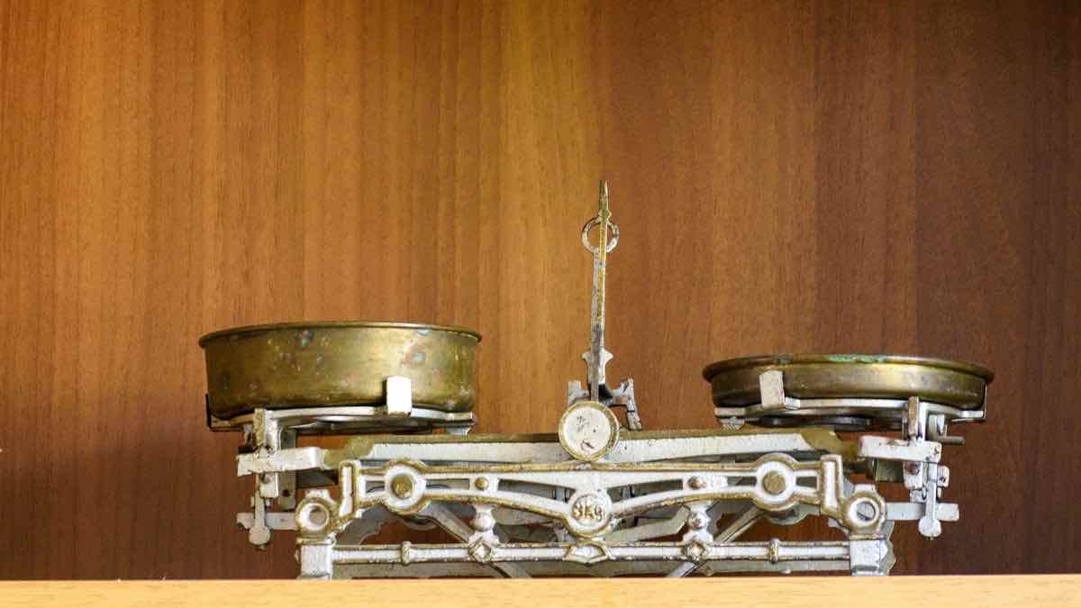 A brass balance scale on a wooden shelf, its two pans holding visibly different loads